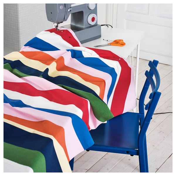 Ljust flerfärgat randigt tyg draperat på blå stol nära symaskin.