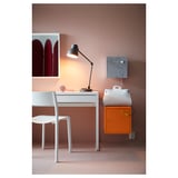 Mysigt hemmakontor med vit JANINGE stol, rent skrivbord, lampa och orange skåp mot brun vägg.