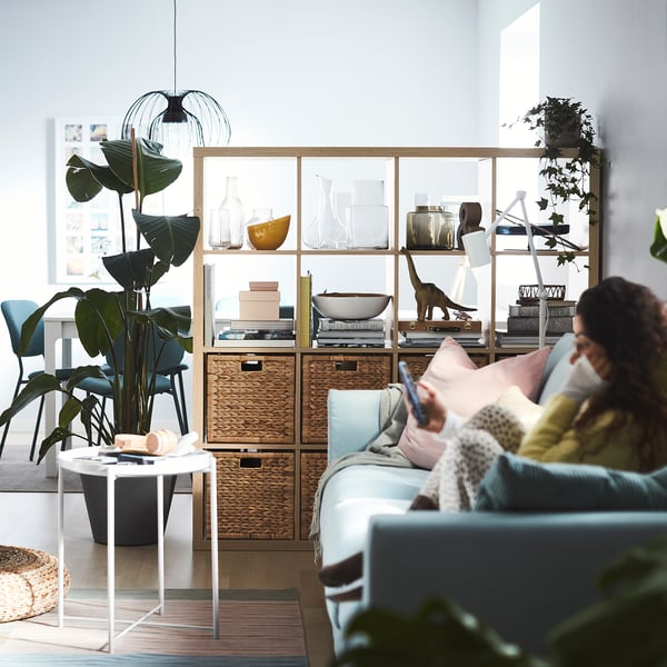 Ett mysigt vardagsrum med en hylla KALLAX, blå soffa och en stor växt.