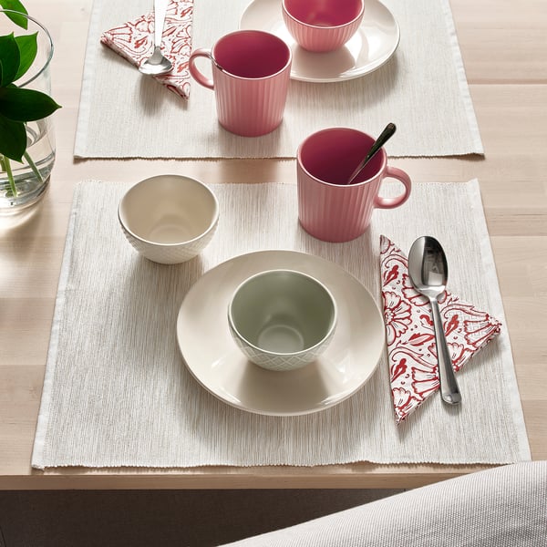 Bordsdukning med rosa muggar, grön skål, vit tallrik, skedar och mönstrade servetter på beige bordstabletter.