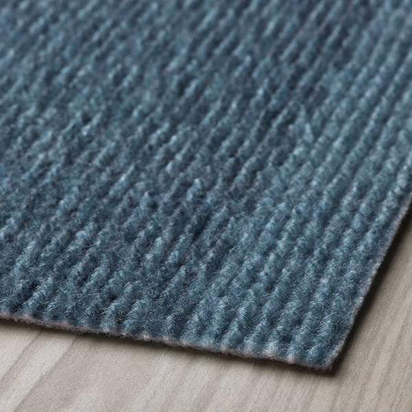 Närbild av en texturerad blå dörrmatta på ett ljust golv som visar upp dess hållbara, återvunna material med ett subtilt mönster.