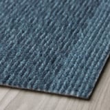 Närbild av en texturerad blå dörrmatta på ett ljust golv som visar upp dess hållbara, återvunna material med ett subtilt mönster.