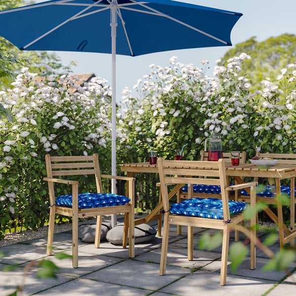 Uteservering med blå och vita prickiga kuddar på trästolar, blått paraply, omgivet av vita blommor.