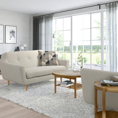 Modernt vardagsrum med ljus soffa, soffbord, stora fönster, matta, fåtölj och växt.