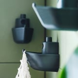 Svarta väggkrokar formade som båtar av återvunnet material i badrumsmiljö, med vitt garn och en handduk i handen.