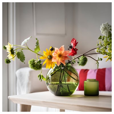Frodiga blommor i rund grön glasvas på bordet.