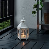 En liten vit lykta står på ett mörkt träbord och kastar ett varmt ljus genom sitt blommiga mönster.