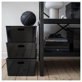 Staplade KUGGIS-lådor med handtag, basketboll på toppen, hylla med böcker och lampa bakom.