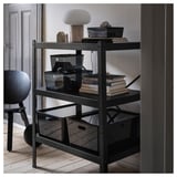 Hylla i svart metall med olika föremål inklusive lampa, lådor och böcker. Modern och minimalistisk design.