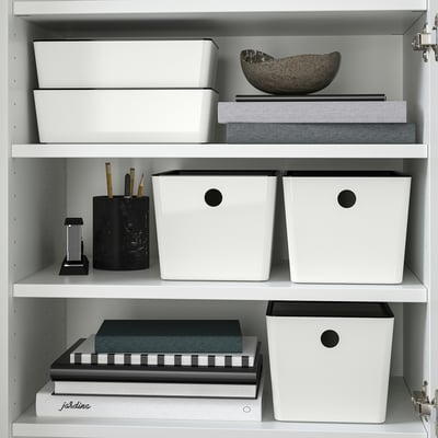 Hylla med KUGGIS-lådor för förvaring av föremål, stapling säkert med lock och en kopp med skrivverktyg.