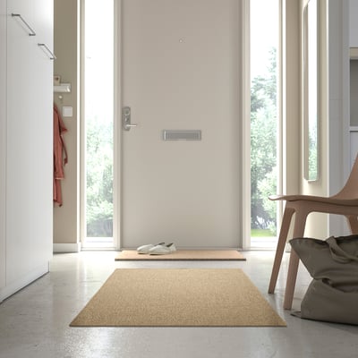 Beige matta LÄTTBETONG i hallen, nära dörr och stol, kompletterar den minimalistiska inredningen.