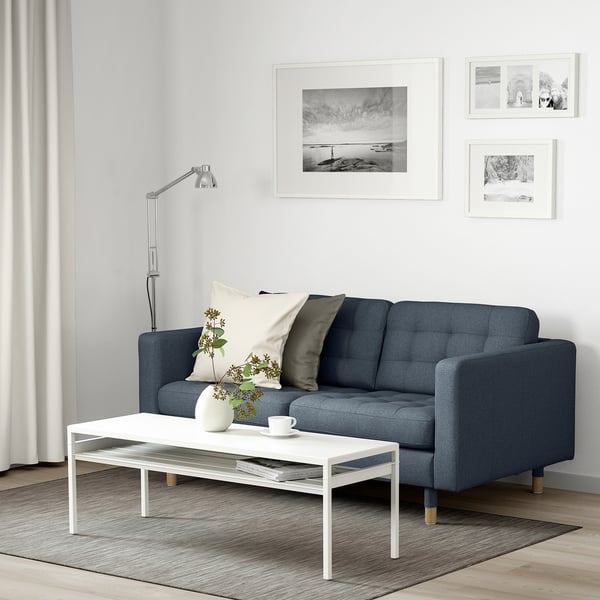 Ett mysigt vardagsrum med en blå tygklädd soffa, vitt soffbord och golvlampa.