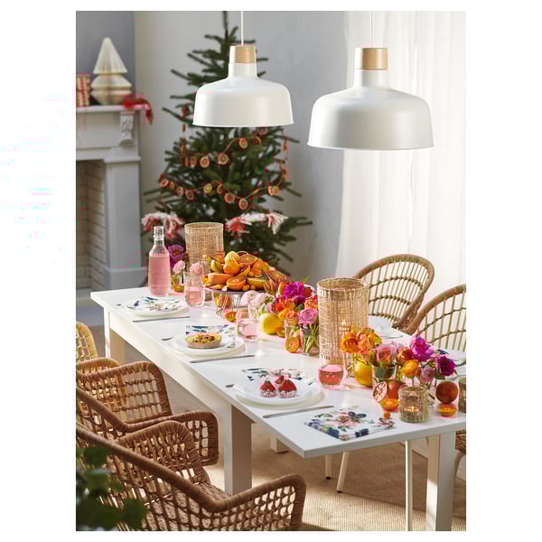 Festlig matscen med vitt LANEBERG-bord, korgstolar, hängande lampor, dekorerad julgran och färgglada blommiga mittpunkter.