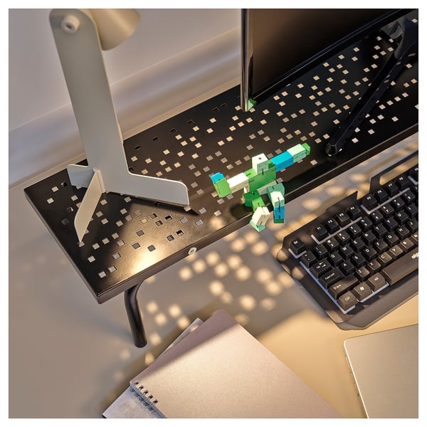 Datorbord med bildskärmsstativ, tangentbord och färgglad robotleksak.