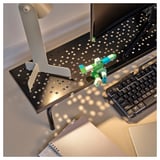 Datorbord med bildskärmsstativ, tangentbord och färgglad robotleksak.
