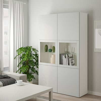 Stort skåp LAPPVIKEN med grå front, glasdörrar. Modern, elegant design, placerad mellan gardiner och en soffa, med dekorativa föremål.