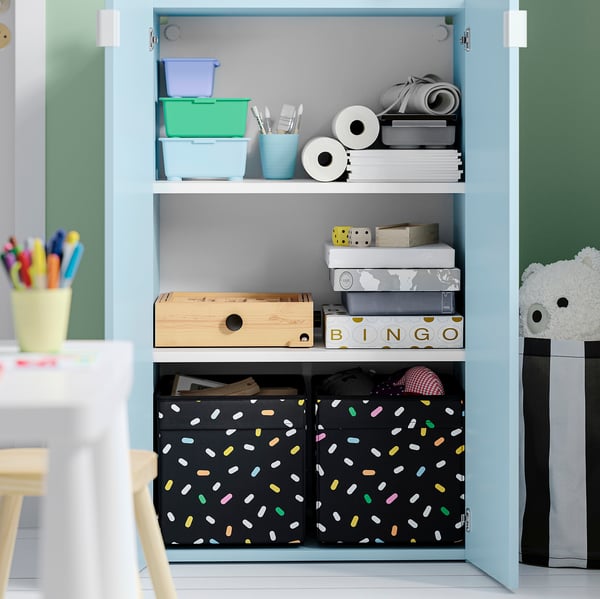 Öppet ljusblått förvaringsskåp med lådor och kontorsmaterial, inklusive färgglada pennor och pappersrullar.