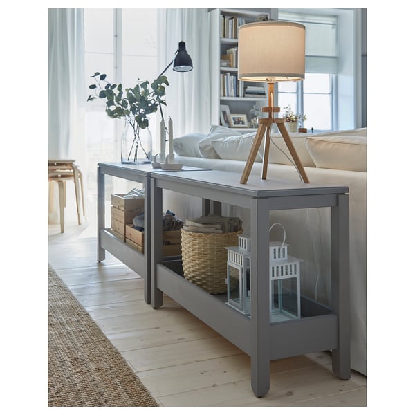 Modernt vardagsrum med grått LAUTERS-bord med lampa, böcker och inredning. Ljusa trägolv, ljusa fönster.