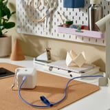 En vit usb-c-laddningskabel med en blå sladd och fäst elastiskt band för organiserad förvaring, placerad på en arbetsyta av korkmatta.