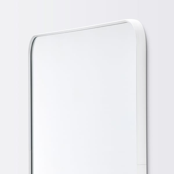 Modern rektangulär spegel med elegant vit ram, monterad på väggen, reflekterar ljus för ett rent, minimalistiskt utseende.