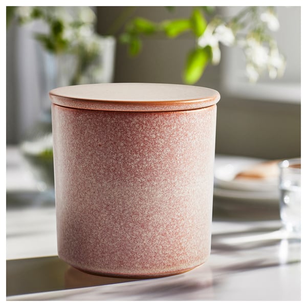LUGNARE rosa ljus i rosa keramikburk och lock. Rund form med spräcklig glasyrdesign. Ställ på ett bord med suddig grönska.