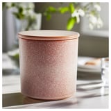 LUGNARE rosa ljus i rosa keramikburk och lock. Rund form med spräcklig glasyrdesign. Ställ på ett bord med suddig grönska.