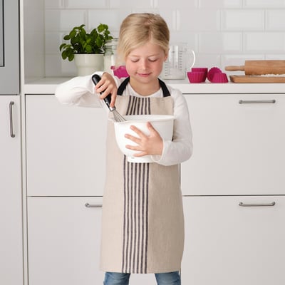 Flicka i randigt förkläde använder stavmixer i köket.