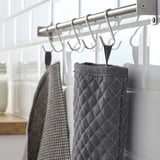 En köksdel med upphängningskrokar som visar gråa texturerade ugnsvantar och en rutig handduk, organiserad för enkel åtkomst.