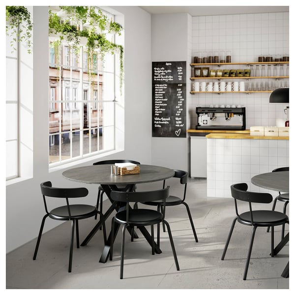 Modernt kafé med MARIEDAMM svarta metallbord och stolar, vita kaklade väggar, stora fönster och svart tavelmeny.