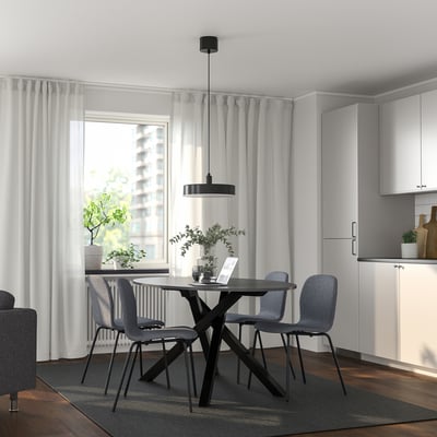 Modern matsal med runt bord, gråa stolar, pendellampa, vita gardiner, minimalistiskt kök.