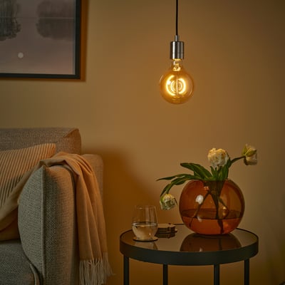 Mysigt rum med MOLNART glödlampa, röd vas och blommor, glas, beige filt, inramad konst, varmt ljus.