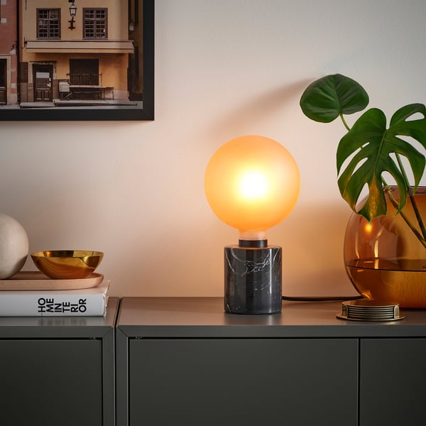 Modernt vardagsrum med MOLNART-lampa, frostbrun glödlampa på marmorbas, placerad bredvid stora växt- och inredningsartiklar.