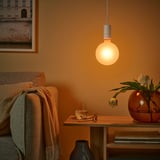 Ett mysigt vardagsrum med en MOLNART-lampa som kastar ett varmt sken, nära en soffa med en filt och sidobord med vatten, glas och blommor.