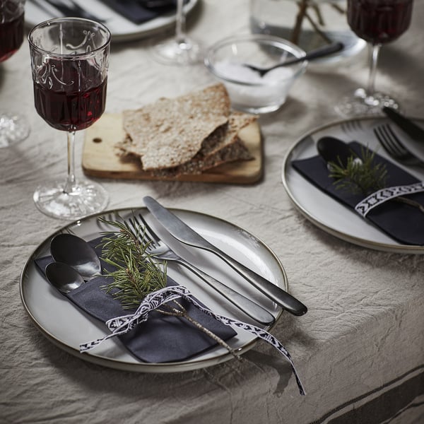 Dukning med MOTTAGA servetter, bestick, vinglas och brödskivor.