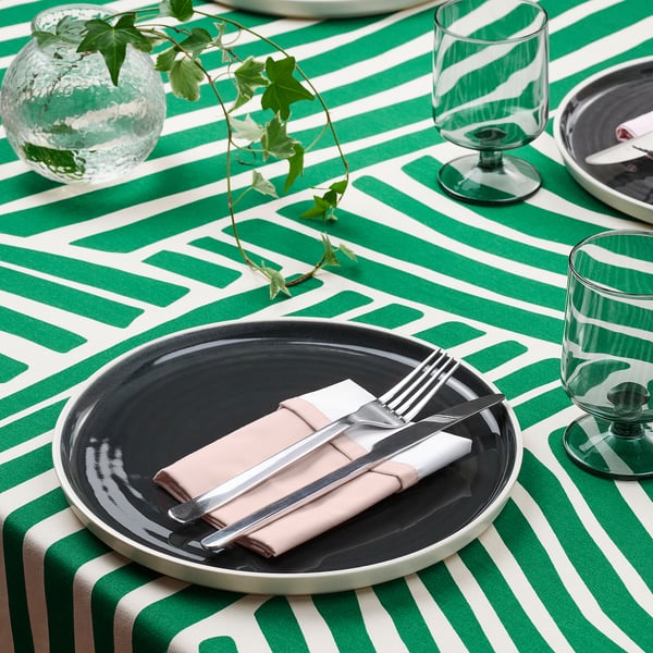 Grön- och vitrandig dukning med mörka tallrikar, rullade bestick i servett och glas.