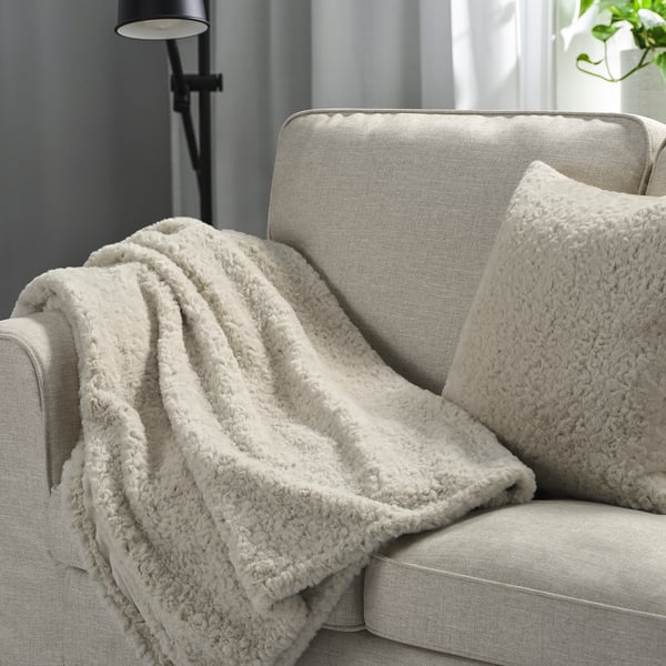 Beige NÄTNÄVA filt och kudde på grå soffa som skapar en mysig atmosfär.