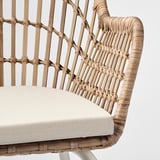 Närbild av en flätad rottingfåtölj med beige dyna som visar upp ett intrikat hantverk.