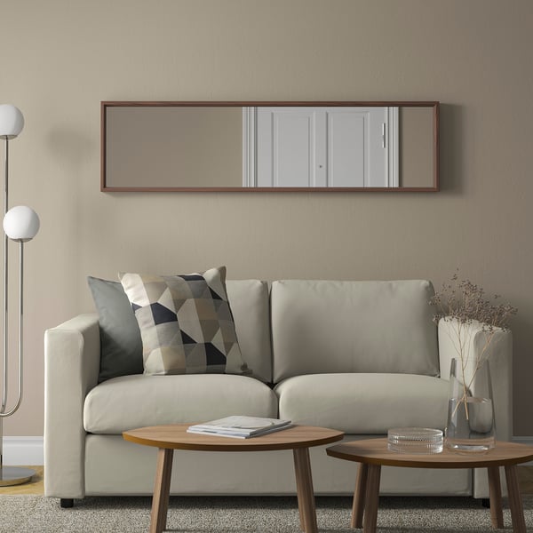 Litet vardagsrum med stor spegel, ljusgrå soffa, runda träbord, golvlampa och dekorativ vas.
