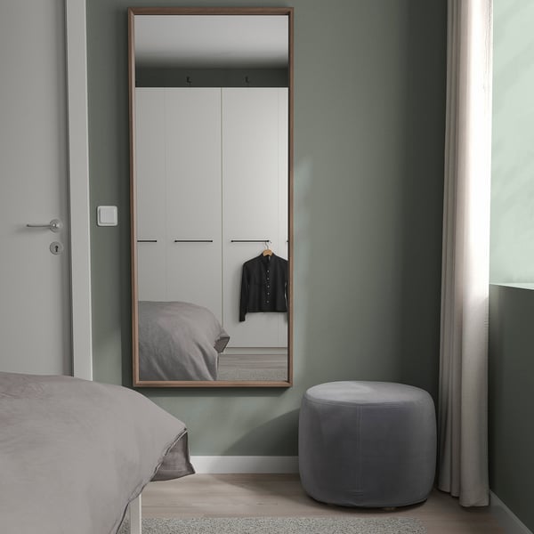 Minimalistiskt sovrum med NISSEDAL spegel, säng, ottoman, dämpade gröna väggar, garderob.