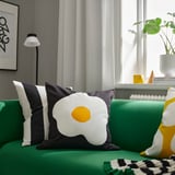 Tre kuddar på grön soffa; mitten med solsidan upp design.