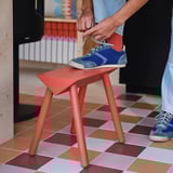 Person som knyter blå sneakers medan han sitter på en röd, triangulär pall.