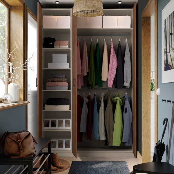 En modern garderob med vikbara dörrar. Inuti organiserar hyllor kläder och accessoarer. Naturligt ljus strömmar in och förstärker den varma inredningen.