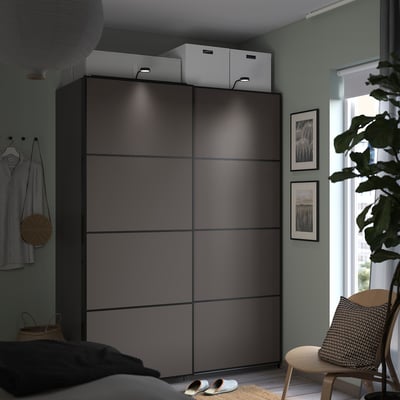 En modern inredning, en elegant grå PAX-garderob med minimalistiska skjutdörrar, stylad med gröna väggar och naturliga inredningselement.