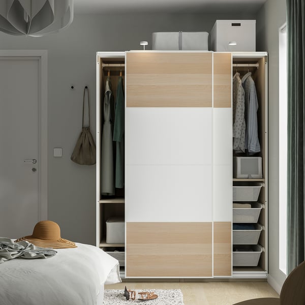 Modern garderob med skjutdörrar, hängande kläder, hyllor och förvaringskorgar i sovrumsmiljö.