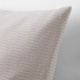 Närbild av ett beige kuddfodral med subtil randig textur som visar upp mjuk, vävd bomullskvalitet.