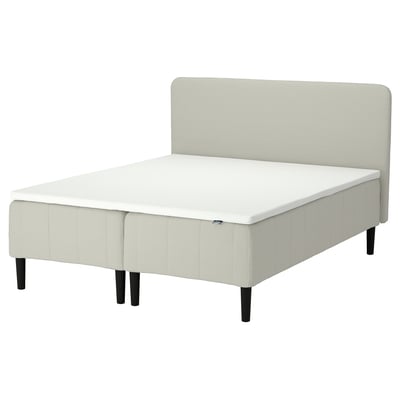 En RÅHOLMAR säng med vit madrass och beige stoppad sänggavel och botten med mörka ben.
