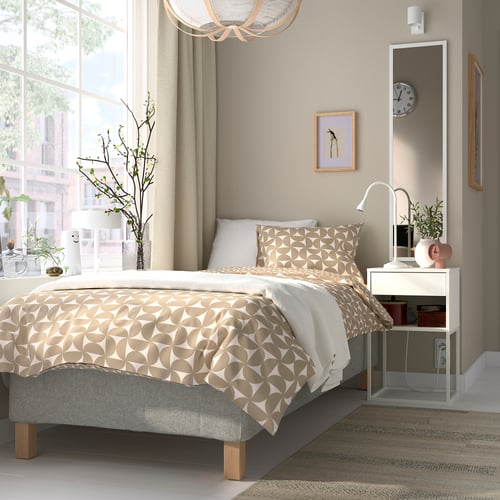 Sängen RÅHOLMAR : neutral geometrisk beige-vit, robust träram, 5 komfortzoner, hög sänggavel, med vitt nattduksbord och inredning.
