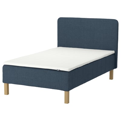 En marinblå IKEA RENFJÄLLET-säng med ljusa träben, en vit madrass och matchande sänggavel. Sängen är klädd i mörkblått tyg.