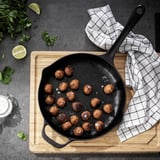 En gjutjärnspanna med köttbullar, örter, lime och salt på en träbräda med en rutig handduk.