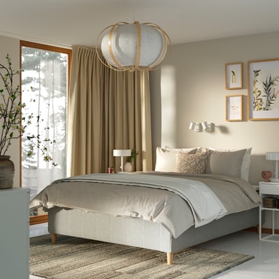 Modern sovrum med beige RISHÖJDEN-säng, mjuk belysning och naturmönster. Sängarnas beige linne kontrasterar mot ljusa gardiner och framhäver mysiga, naturliga toner.